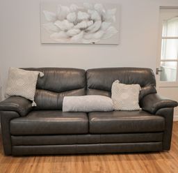 A dark leather sofa with three cushions and a painting of a flower on the wall behind at Cheviot View in Beadnell