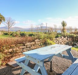 An outdoor picnic table and benches on gravel with stone wall and mountain view at Kates Cottage in Knightstown Valentia Island County Kerry