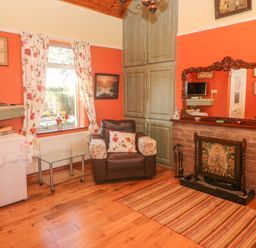 A living room with a brown armchair, floral curtains, a TV, a glass table, a fireplace with a large wooden framed mirror above it at Kates Cottage Knightstown Valentia Island County Kerry