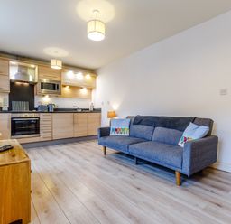 A kitchen with wooden cabinets and appliances next to a living area with a blue sofa and a wooden TV stand at Sunrise The Bay near Filey