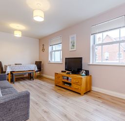 A living room with a gray sofa a wooden TV stand with a television a dining table with chairs and two windows at Sunrise The Bay near Filey