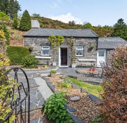 A stone cottage with slate roof and a garden pathway leading to the entrance at Henrhiw Bach in Penmachno