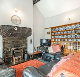A living room with black leather sofas a fireplace and a wooden plate rack with blue and white plates at Henrhiw Bach in Penmachno