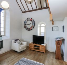 A living room with a television and clock at Eglwys St Cynfil Penrhos near Pwllheli