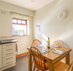 A kitchen dining area with a wooden table set for four and a window with a vase on the sill at Ridge Cottage in Whitridge