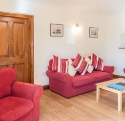 A sitting room with red sofas and striped cushions wooden door and a wooden coffee table at Ridge Cottage in Whitridge