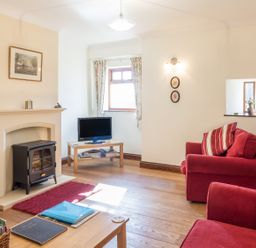 A living room with a fireplace TV wooden furniture and red armchairs at Ridge Cottage in Whitridge