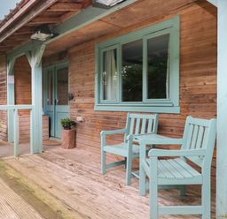 A wooden porch with two mint green chairs and a small table at Timbertwig Lodge in Lamphey near Pembroke