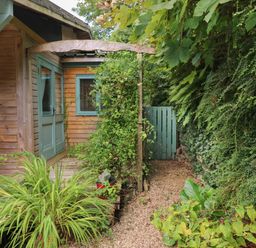 A wooden house with green doors and windows surrounded by plants and a gravel pathway at Timbertwig Lodge in Lamphey near Pembroke