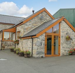 Stone building with wooden framed windows and doors surrounded by flower pots at Pendre Uchaf in Melin-y-Wig near Ruthin