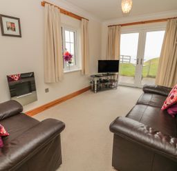 A living room with two leather sofas facing a television and glass doors at White Rock Cottage in Beadnell