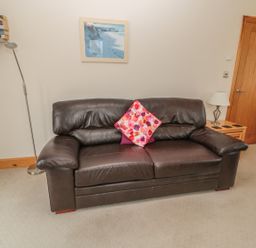 A leather sofa with two cushions in a living room with a wooden door and lamp at White Rock Cottage in Beadnell