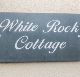 A stone plaque with White Rock Cottage written on it attached to a textured wall at White Rock Cottage in Beadnell