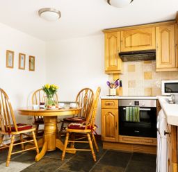 A kitchen with wooden dining table and chairs with tulips on the table and wooden cabinets at The Shippon Near Launceston