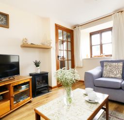 A living room with a blue sofa a wooden cabinet a TV a glass door a table with flowers and cups at The Shippon Near Launceston