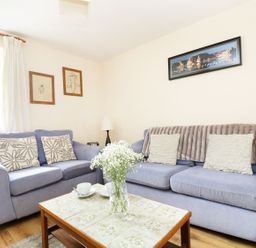 A living room with two blue sofas a coffee table with a vase of flowers and framed pictures on the wall at The Shippon Near Launceston
