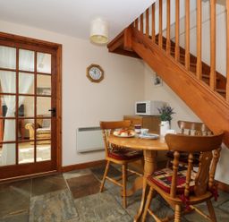 A dining area with wooden table and chairs under a staircase and a glass door with curtains at The Wagon House in Polyphant near Launceston