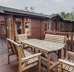 An outdoor wooden deck with wooden table and benches in front of a wooden cabin at Langdale Lodge 15 White Cross Bay near Troutbeck Bridge