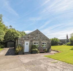 A stone building with two windows and a door a bench and plants outside a green shed driveway and lawn at Drovers Rest in Otterburn