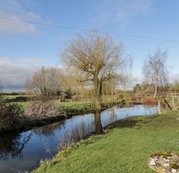 A river with trees and grass along the bank in a rural area at Stables Cottage in Bowerhill near Melksham