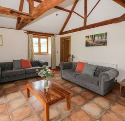A living room with two grey sofas a wooden coffee table with flowers and exposed wooden beams at Beesoni Lodge in Castlemorton near Malvern