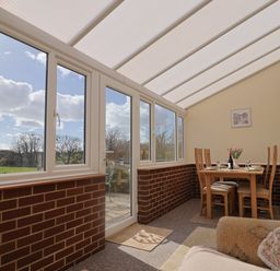 A sunroom with dining table and chairs and windows showing outdoor trees at 1 Cowdea Farm in Bettiscombe near Beaminster and Bridport