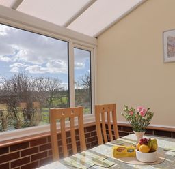 A dining area with wooden chairs a table with fruit and flowers near a large window at 1 Cowdea Farm in Bettiscombe near Beaminster and Bridport