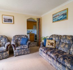 A living room with patterned sofas and pillows and a kitchen visible through an archway at 1 Cowdea Farm in Bettiscombe near Beaminster and Bridport