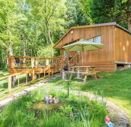 A wooden cabin with a deck and picnic table with umbrella surrounded by trees at Bluebell Cottage in Maenan near Llanrwst