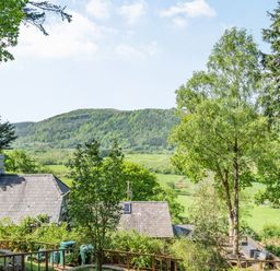 A garden with trees and outdoor seating overlooking fields and a hill at Bluebell Cottage in Maenan near Llanrwst