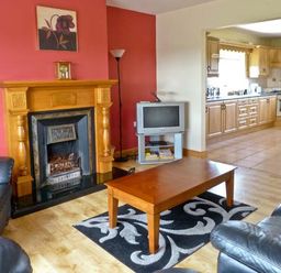 A living room with a fireplace wooden coffee table and black leather sofas next to a kitchen at Sallywood House Carn near Ballybofey County Donegal