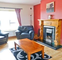 A living room with black leather sofas a wooden coffee table a fireplace with a wooden mantel and a red accent wall at Sallywood House Carn near Ballybofey County Donegal