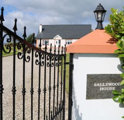 A black metal gate open to a gravel driveway leading to a white house with a dark roof at Sallywood House Carn near Ballybofey County Donegal