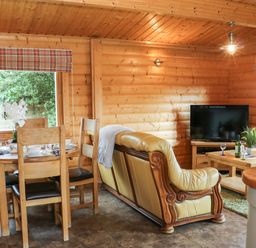 A wooden dining table with chairs and a leather sofa facing a television in a wooden room at Cornfield in Northallerton