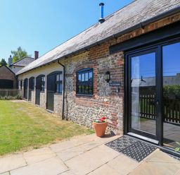 Exterior of a stone and brick building with black doors and windows a small lawn and potted plants at The Old Stables in Winterborne Stickland