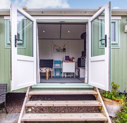 A small porch with open double doors showing a room with chairs and a stove at The Shepherd's Hut in Aberdovey