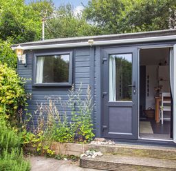 The exterior of a small building with a grey door and window surrounded by plants and greenery at The Shepherd's Hut in Aberdovey