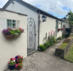 A walkway with flower pots on the ground and flowers in wall-mounted planters outside a white house at Palmers Lodge in Egloskerry near Launceston