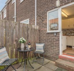 An outdoor patio area with two chairs and a small round table with flowers and a bottle at Crumstone Corner in Seahouses