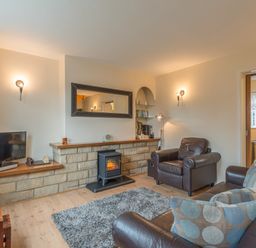 A living room with leather armchairs a rug a small stove and a television at Crumstone Corner in Seahouses