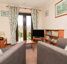 A sitting room with two sofas a wooden coffee table a TV and bookshelves at Honeysuckle Cottage in Bude