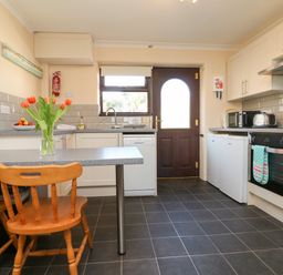 A kitchen with wooden chairs a countertop with flowers a dishwasher a door and various appliances at Honeysuckle Cottage in Bude