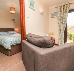 A bedroom with a bed next to a living area with a sofa and glass doors at Honeysuckle Cottage in Bude