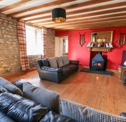A living room with stone walls wooden beams two black sofas and a fireplace with a red wall at The Farmhouse in Aberaeron