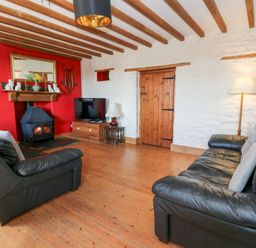 A living room with two black leather sofas a wood stove on red wall and a grandfather clock at The Farmhouse in Aberaeron