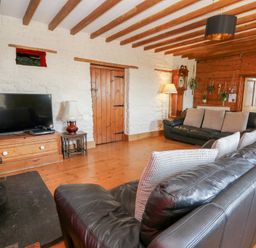 A living room with two black leather sofas a wooden floor and a television at The Farmhouse in Aberaeron