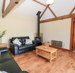 A living room with a sofa, coffee table, and stove at Corner Barn in Winterborne Stickland