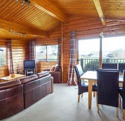A wooden interior living room with a brown leather sofa a television and a dining table with black chairs at Ty Pren in Llanrhian near St Davids