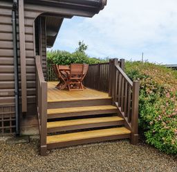 An outdoor wooden deck with stairs and a table with chairs beside a garden at Ty Pren in Llanrhian near St Davids