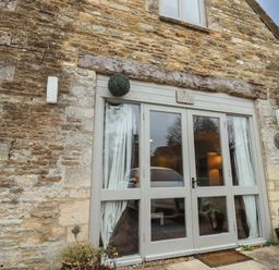 The exterior entrance with glass double doors and stone walls at Greyhound Barn Barnsley near Cirencester